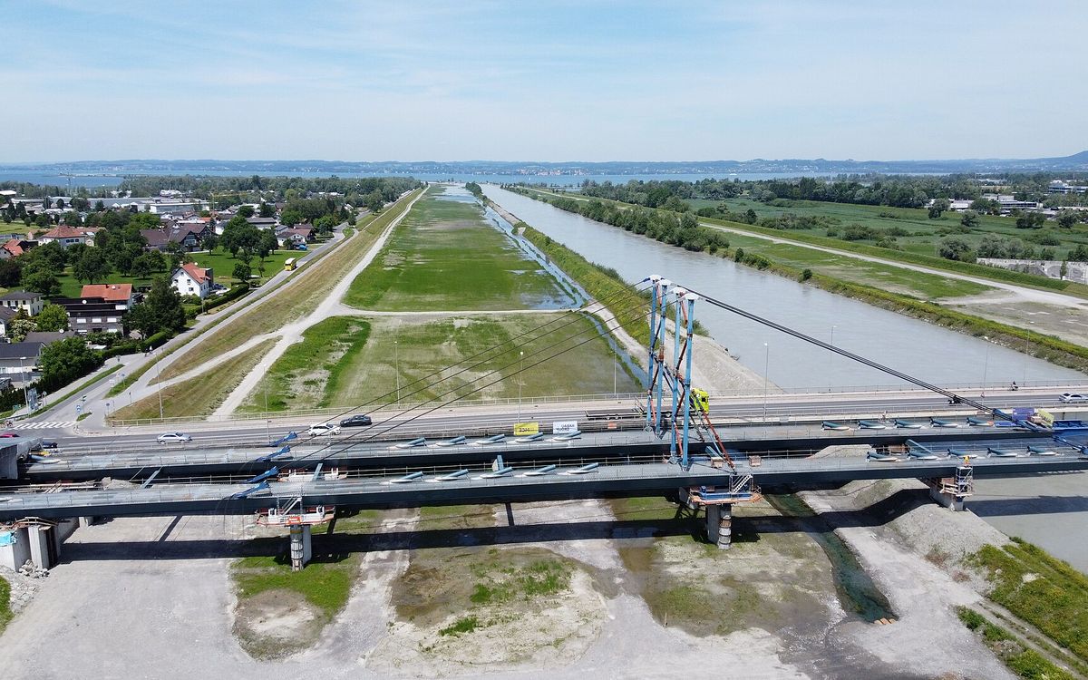 Drone view of a new bridge being built across a river, with cranes and steel girders on the deck